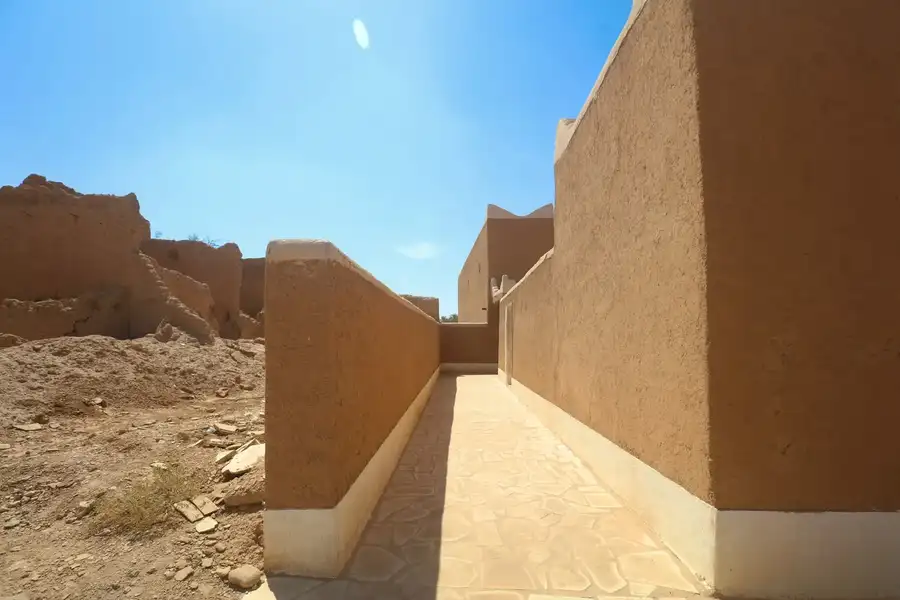 ممر مرصوف بالحجر بين جدارين طينيين مرممين وبجانبه أطلال