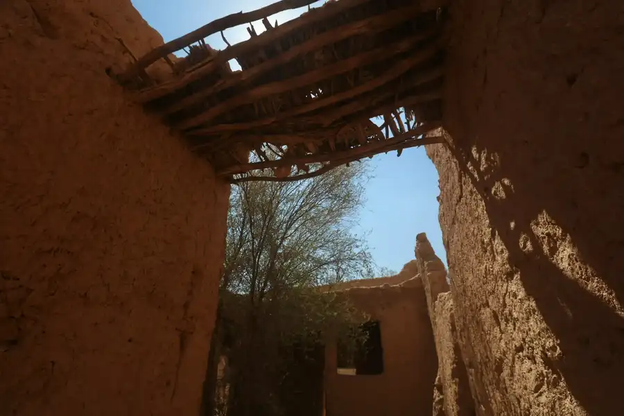 سقف من جذوع النخل والجريد فوق ممر بين جدارين طينيين
