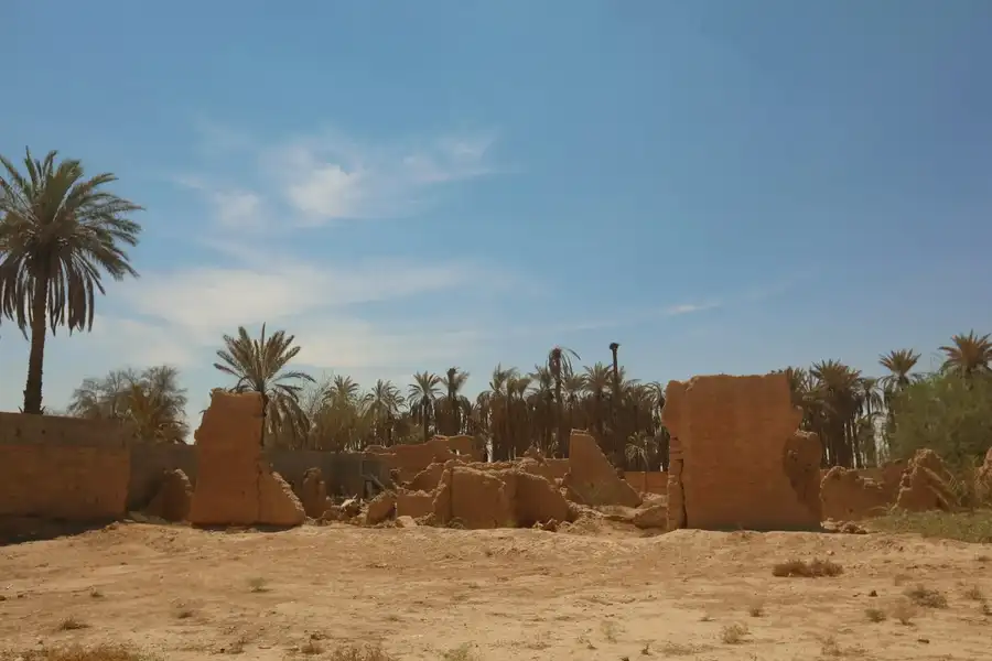 أطلال طينية ونخيل تحت سماء غائمة