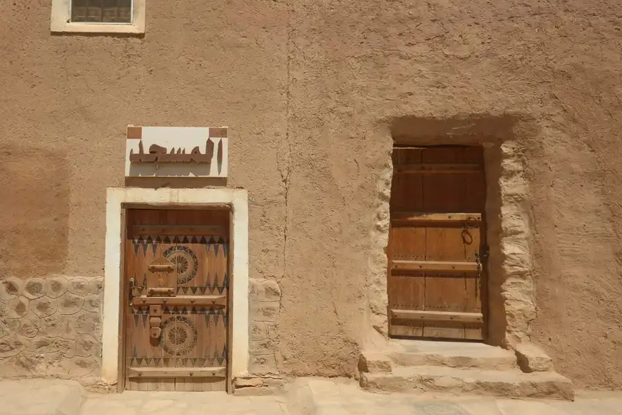 باب خشبي منقوش تعلوه لوحة المسجد، وإلى جانبه باب خشبي قديم